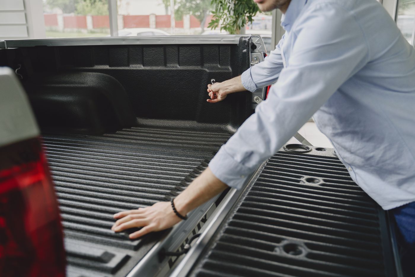 A man rests his hand on the ribbed drop-in bed liner of a new pickup with the tailgate open